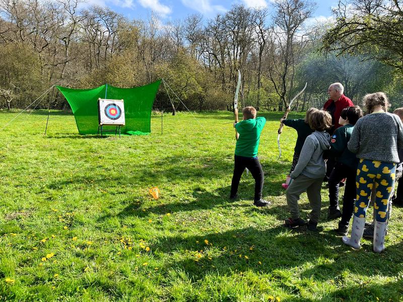 Young people taking turns at archery on a camp field.
