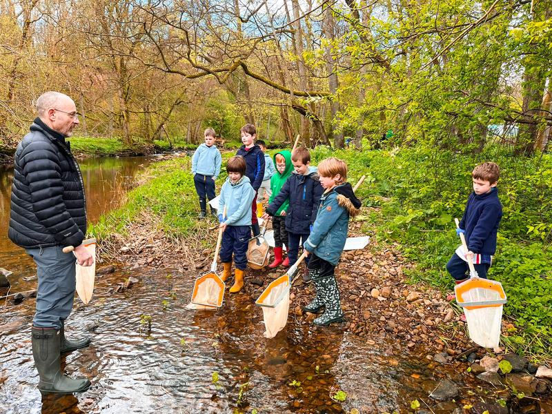 A leader and a group of young people pond-dipping with nets in a shallow river.