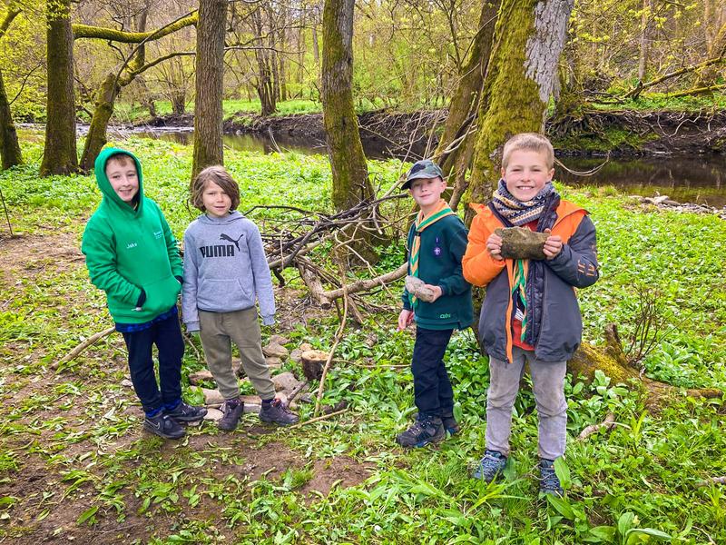 Four young people standing in the woods by a river at camp.